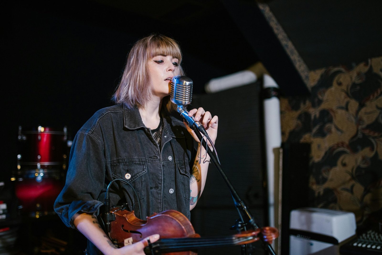 Woman singing while holding a violin on stage with a vintage microphone.